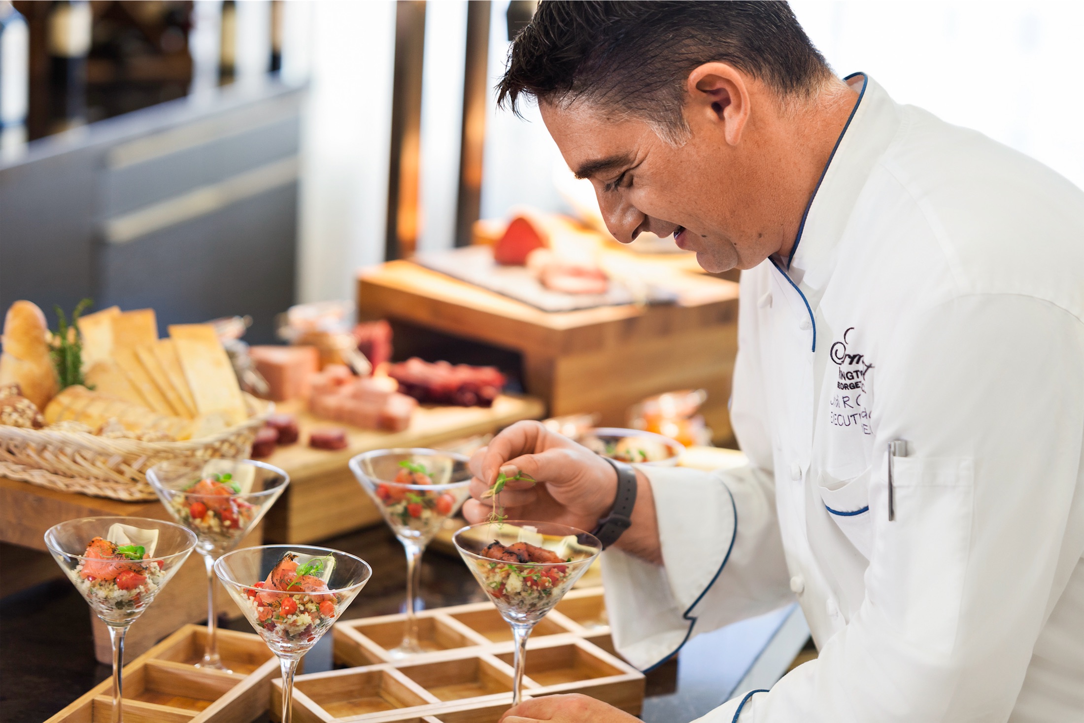 A chef in a kitchen garnishing martini glasses filled with ceviche.