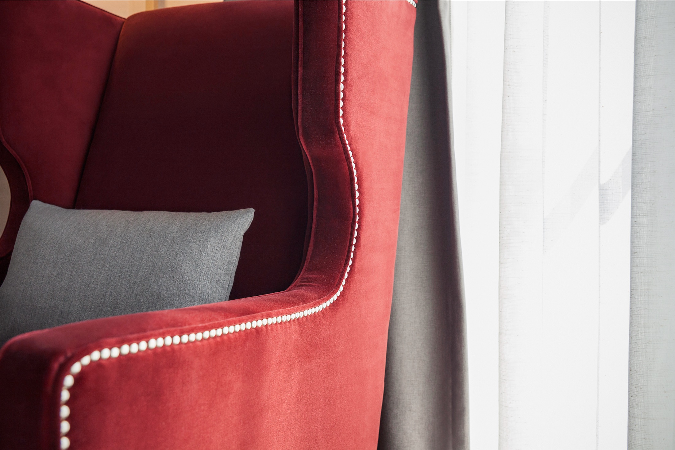 A red wingback armchair with a grey throw pillow