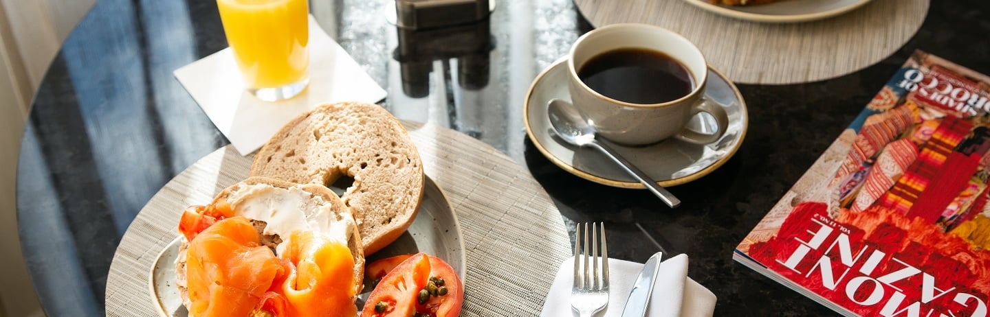 bagel with cream cheese and salmon on a plate next to a cup of coffee