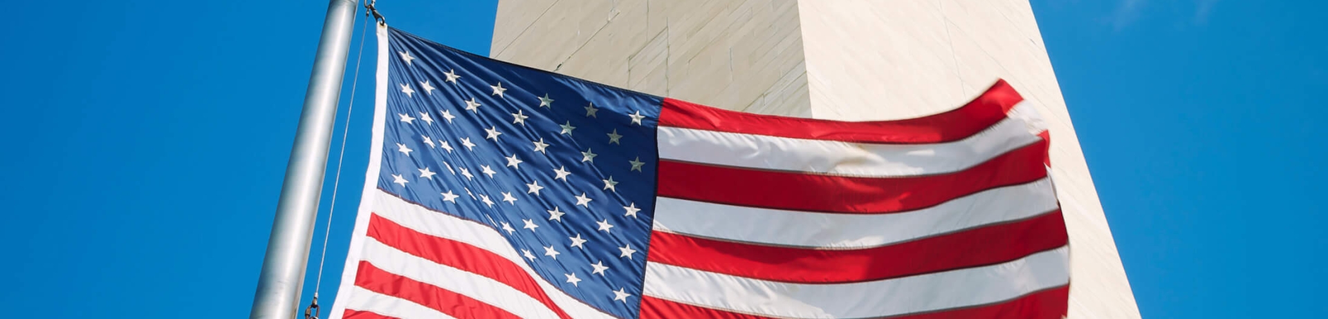 An upward view of a US flag in front of the Washington Monument.