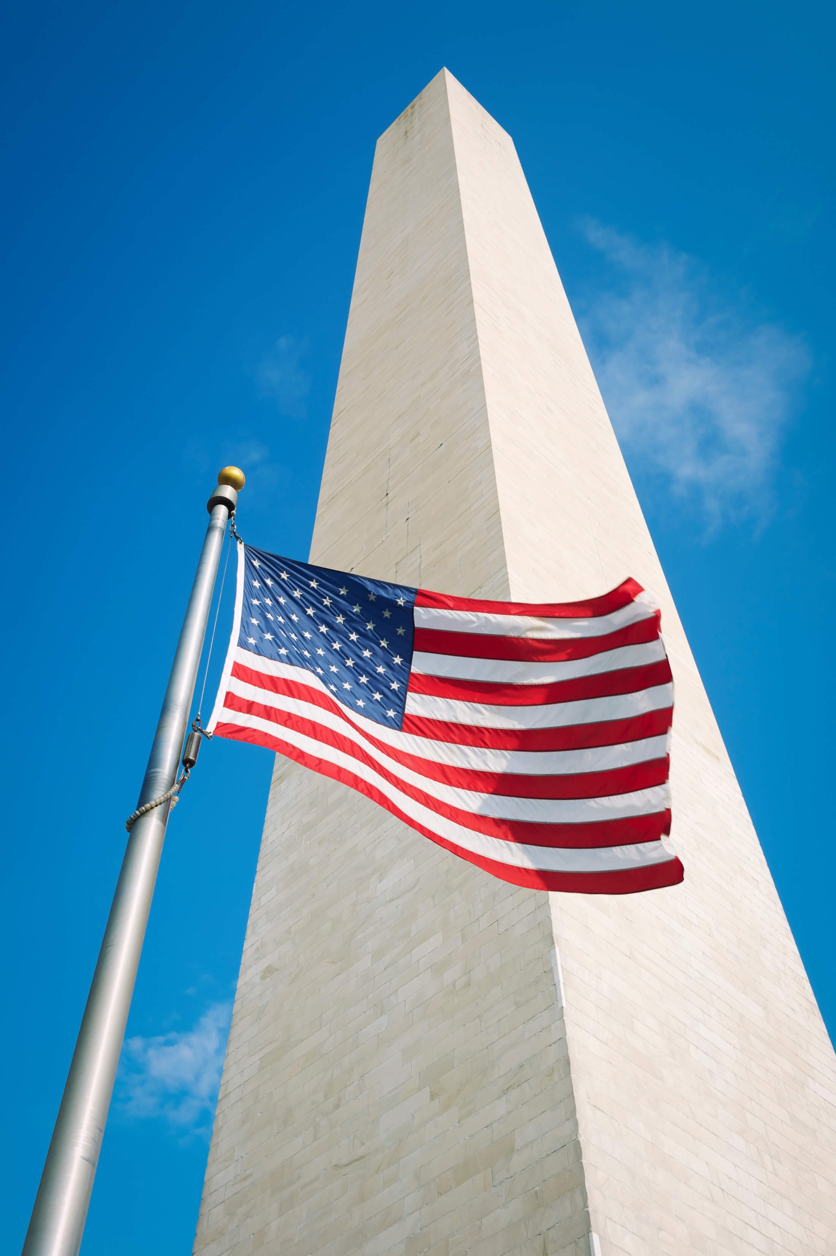 An upward view of a US flag in front of the Washington Monument.