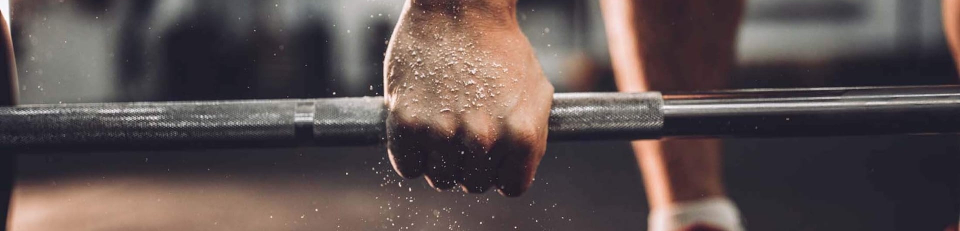 A close up of a power lifter's hand grabbing a barbell.