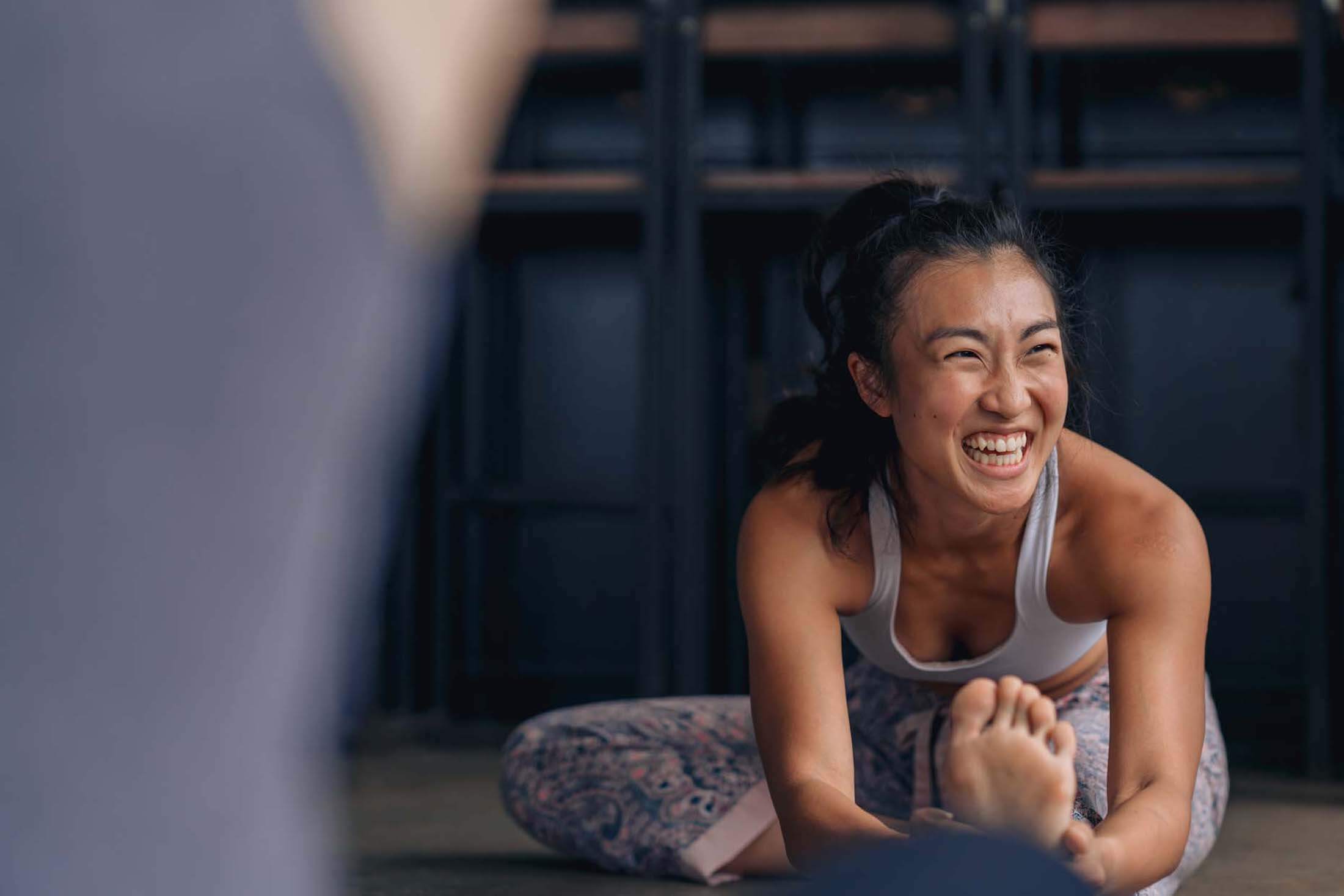 A woman stretching on the floor and laughing.
